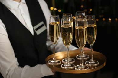 Waiter holding tray with glasses of champagne on blurred background, closeup