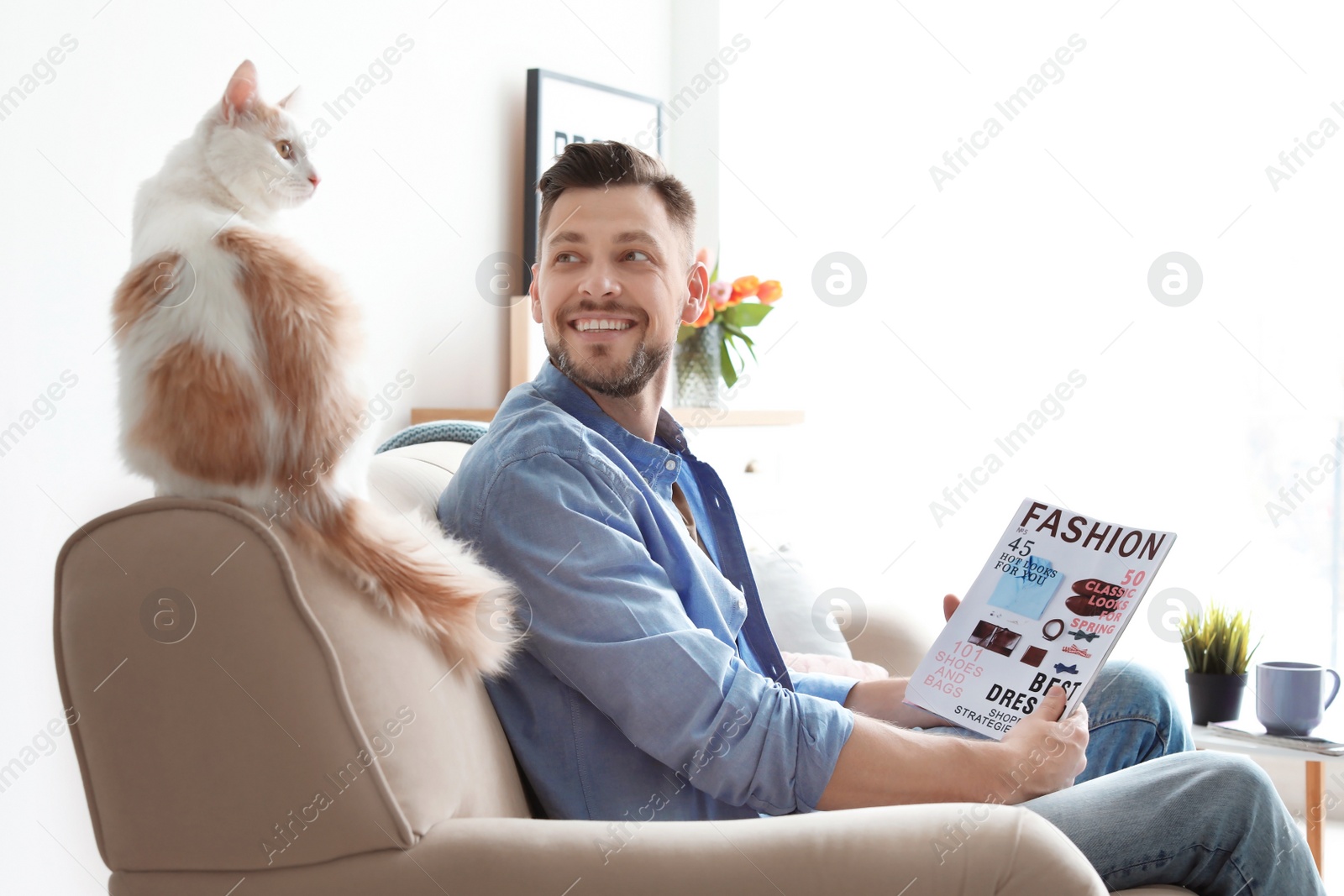 Photo of Young man with cute cat on sofa at home