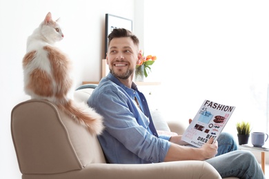 Young man with cute cat on sofa at home