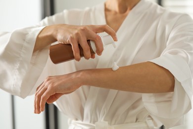 Photo of Woman applying self-tanning product onto arm indoors, closeup