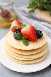 Photo of Stack of tasty pancakes with fresh berries, mint and honey on light grey table, closeup