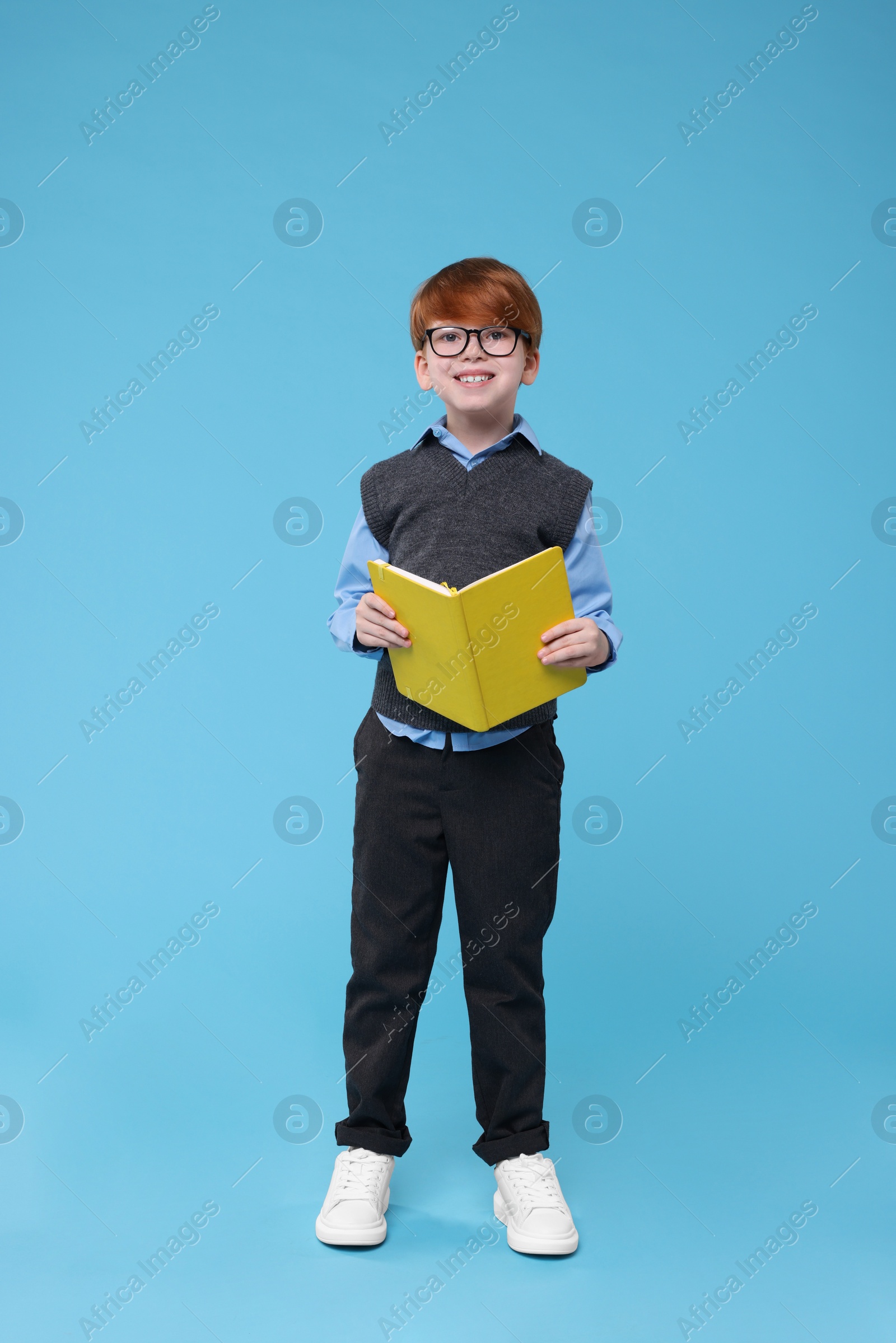 Photo of Smiling schoolboy in glasses with book on light blue background