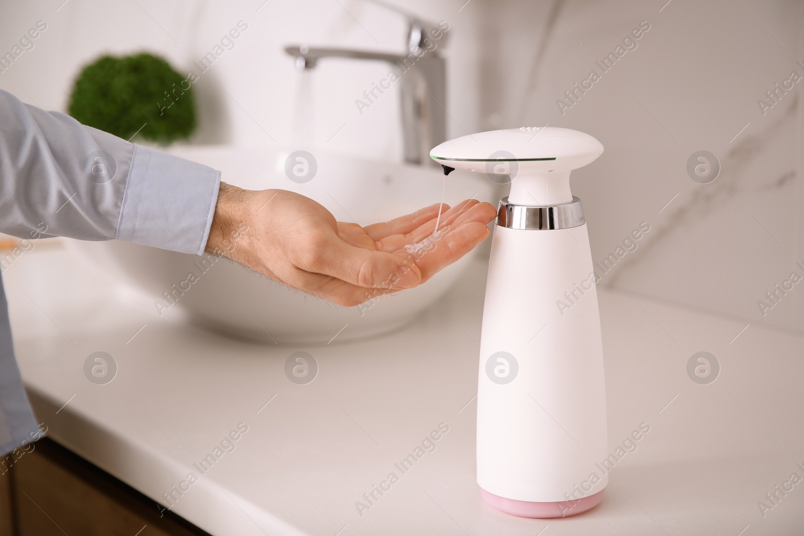 Photo of Man using automatic soap dispenser in bathroom, closeup