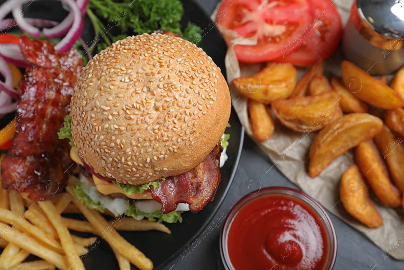 Photo of Fresh juicy bacon burger and fries on grey table, above view