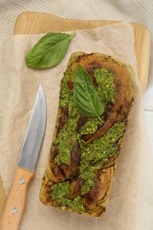 Freshly baked pesto bread with basil and knife on white table, flat lay