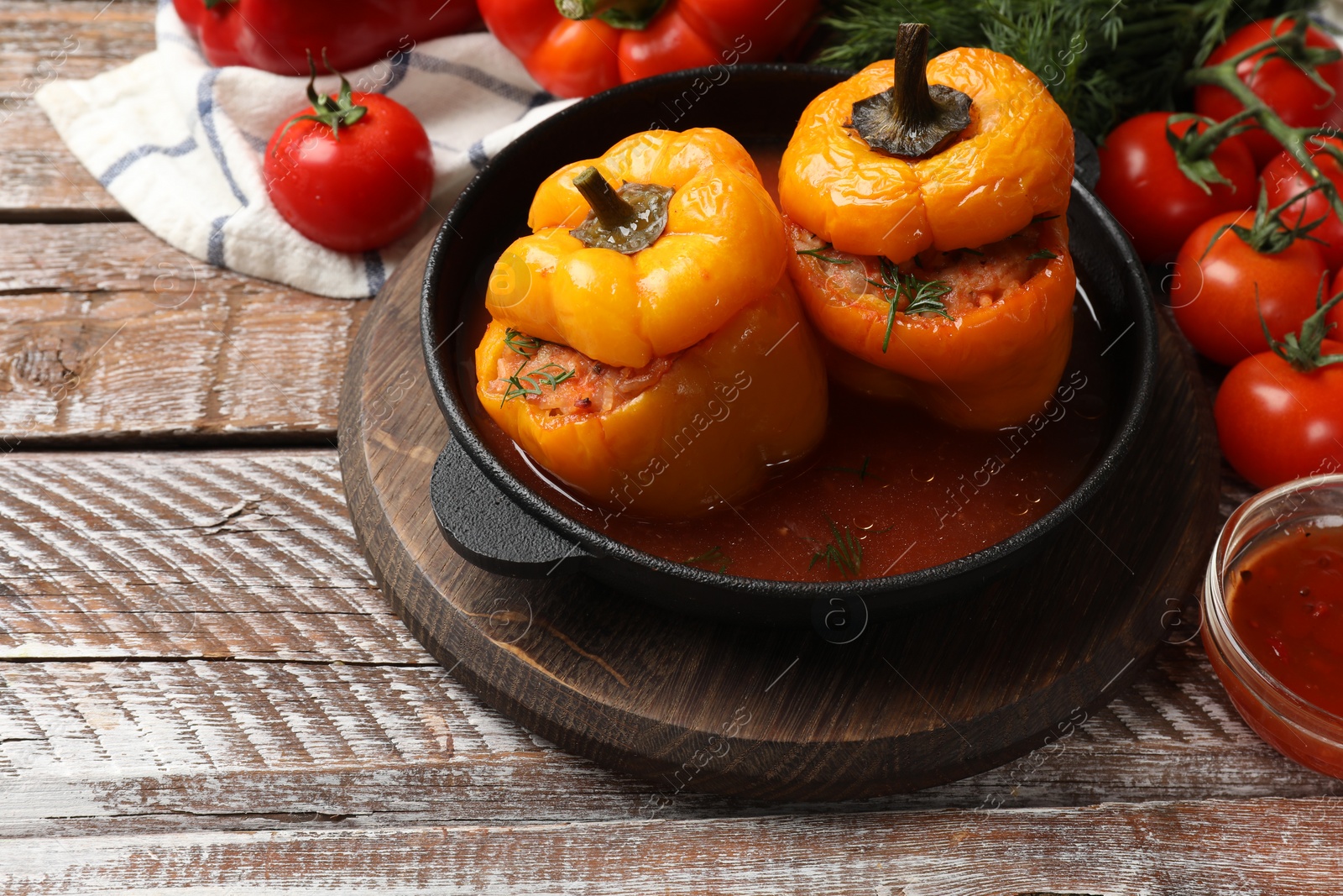 Photo of Tasty stuffed peppers in pan and products on wooden rustic table, closeup