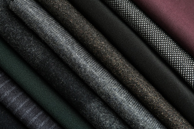 Photo of Stack of different fabric samples as background, closeup. Textile texture