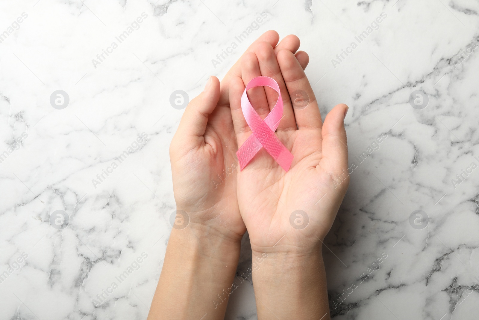 Photo of Woman holding pink ribbon on marble background, top view. Breast cancer awareness concept