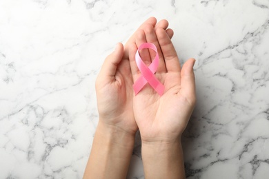Photo of Woman holding pink ribbon on marble background, top view. Breast cancer awareness concept