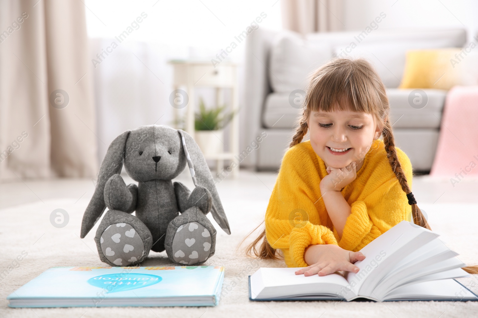 Photo of Cute little girl with toy reading book on floor at home
