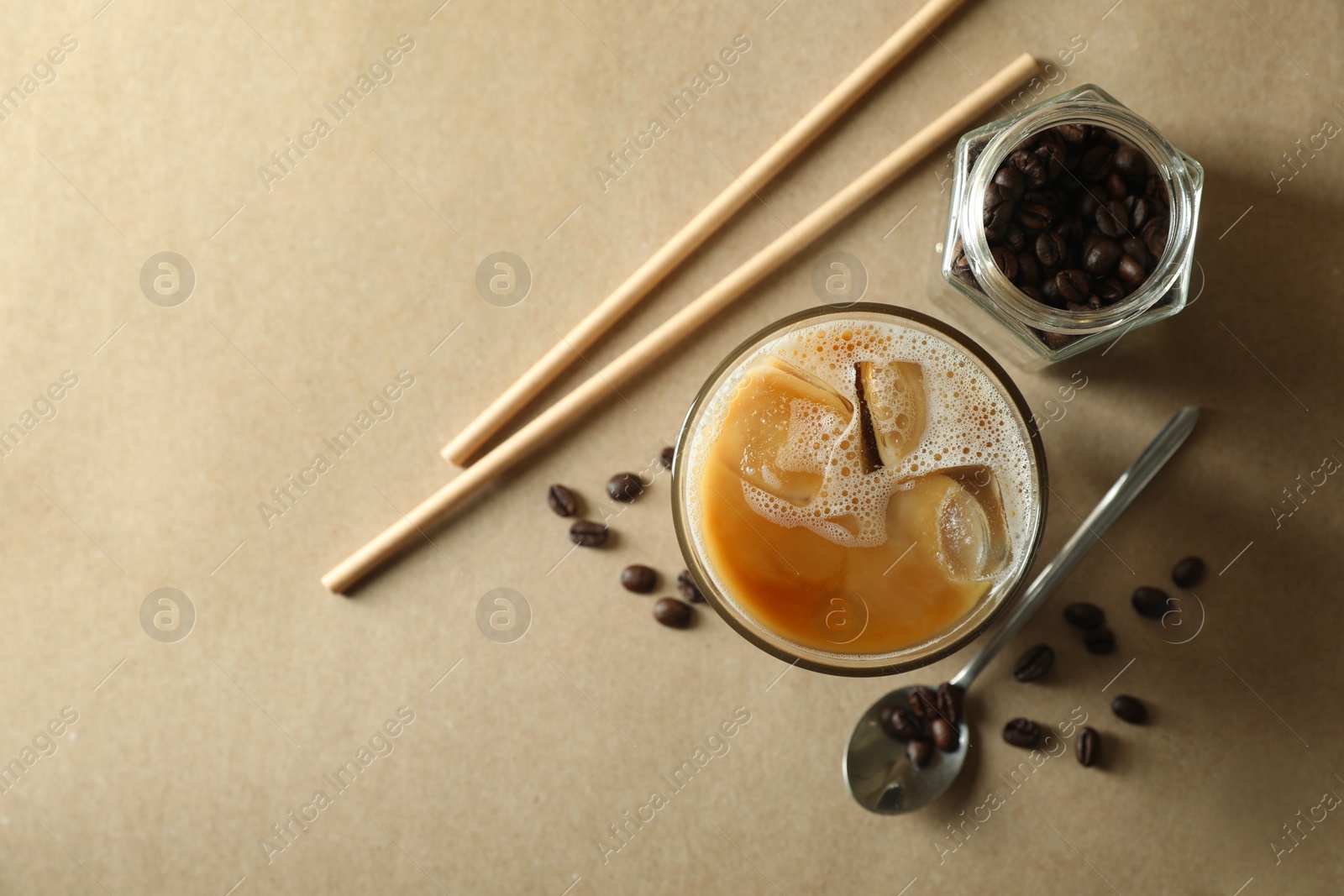 Photo of Refreshing iced coffee with milk in glass, straws and beans on beige background, flat lay. Space for text