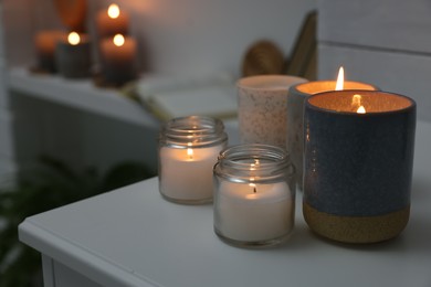 Photo of Burning wax candles on white table in room, space for text
