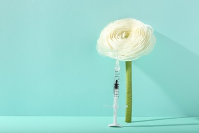 Photo of Cosmetology. Medical syringe and ranunculus flower on turquoise background, space for text