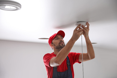 Worker repairing lamp on stretch ceiling indoors