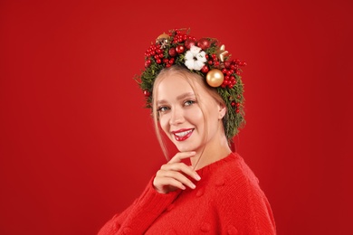 Photo of Beautiful young woman wearing Christmas wreath on red background