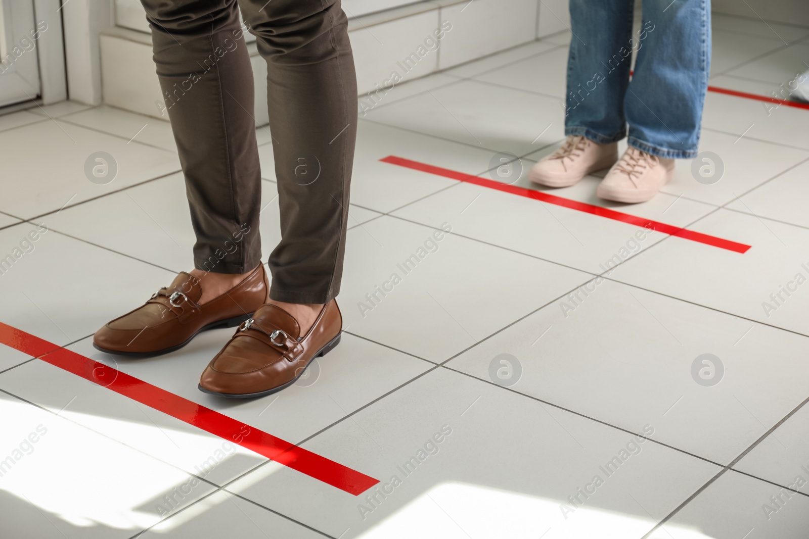 Photo of People standing in line behind taped floor markings for social distance indoors, closeup. Coronavirus pandemic