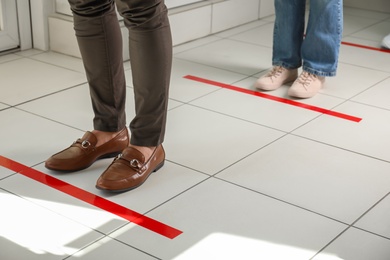 People standing in line behind taped floor markings for social distance indoors, closeup. Coronavirus pandemic