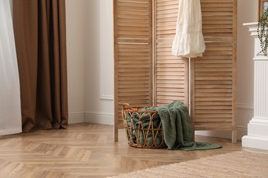 Wooden folding screen and wicker basket with blanket in room. Interior design