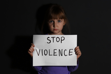 Abused little girl with sign STOP VIOLENCE near black wall