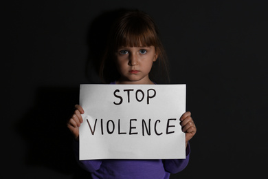 Photo of Abused little girl with sign STOP VIOLENCE near black wall