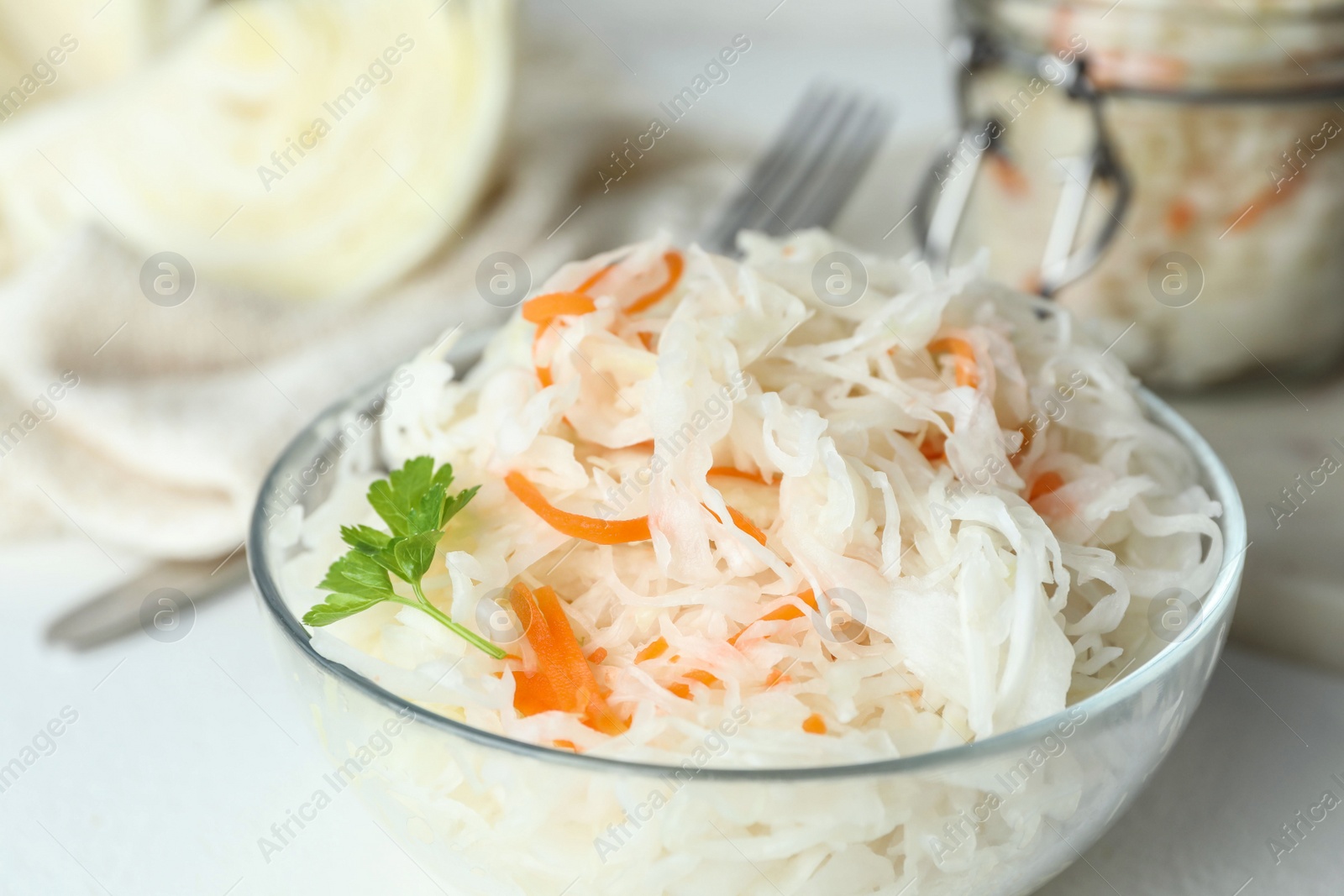 Photo of Glass bowl of tasty fermented cabbage on white table, closeup