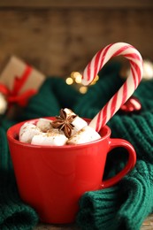 Photo of Cup of tasty cocoa with marshmallows and Christmas candy cane on table