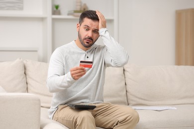 Shocked man with calculator and credit card planning budget at home. Debt problem