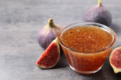 Photo of Bowl with tasty sweet jam and fresh figs on grey table, closeup. Space for text