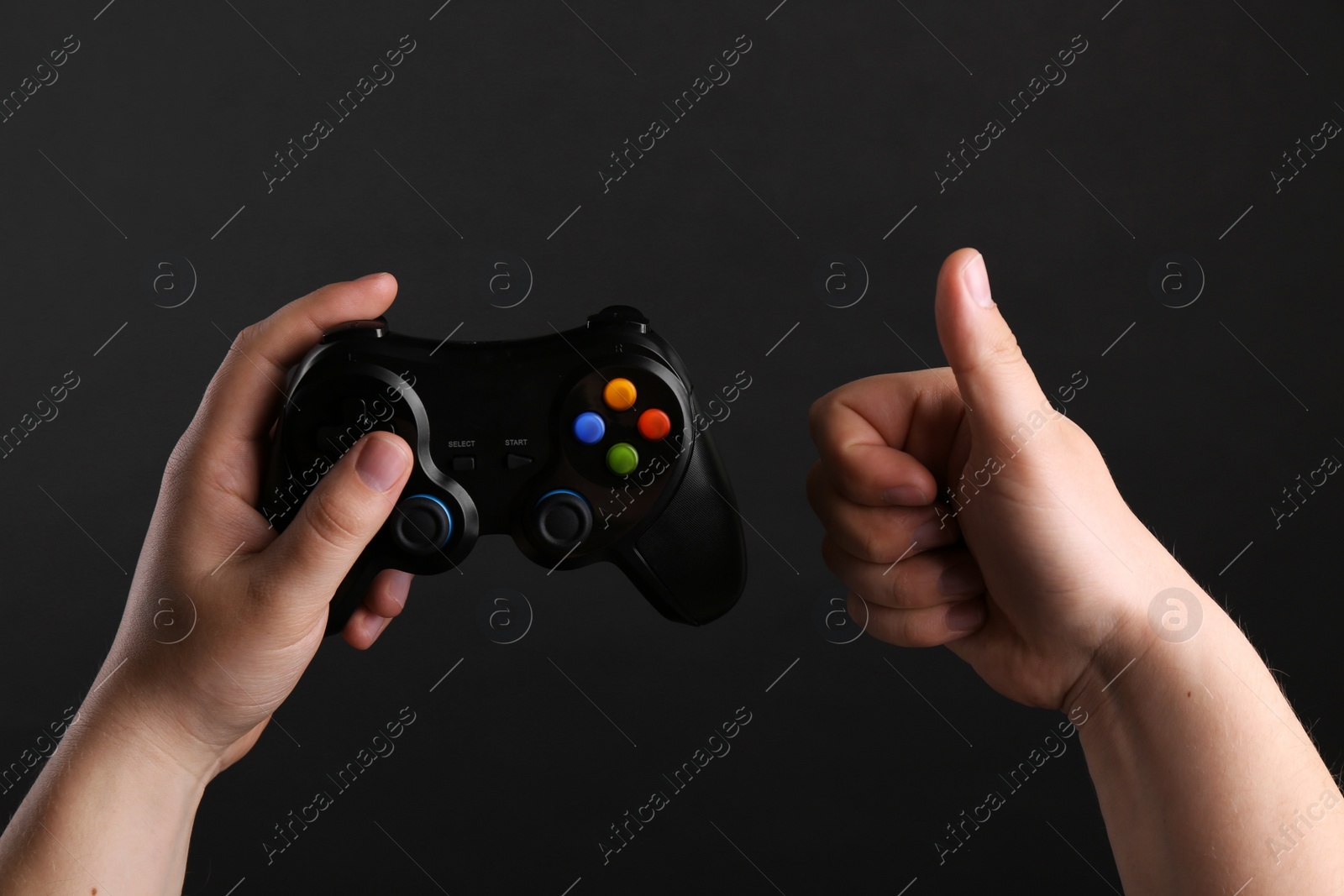 Photo of Woman using wireless game controller and showing thumbs up on dark background, closeup