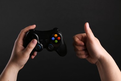 Woman using wireless game controller and showing thumbs up on dark background, closeup