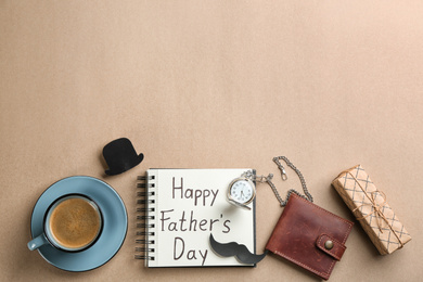 Photo of Notebook with phrase HAPPY FATHER'S DAY, coffee and male accessories on beige background, flat lay. Space for text