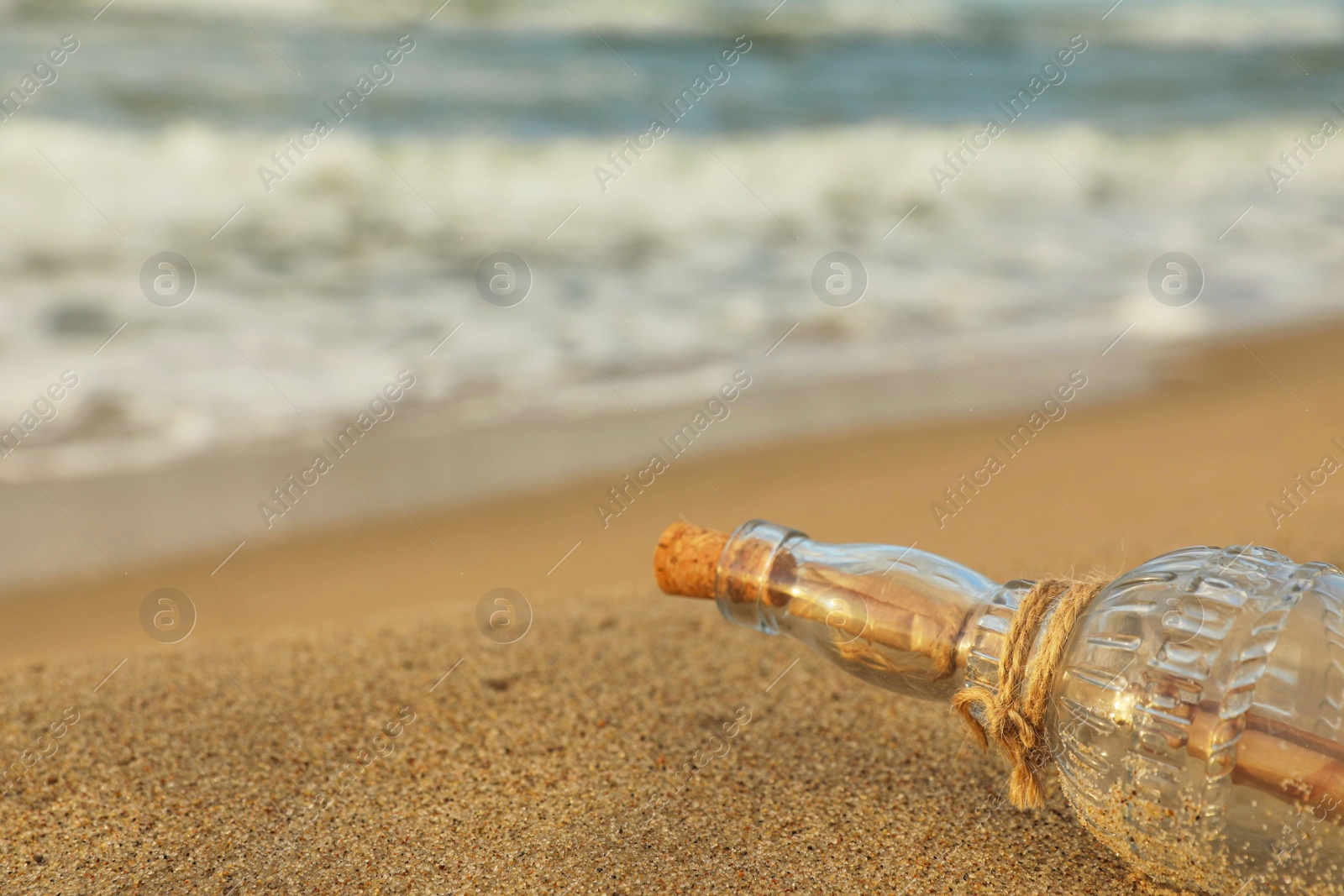 Photo of SOS message in glass bottle on sand near sea, closeup. Space for text