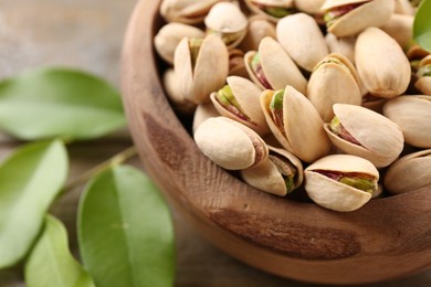 Delicious pistachios in bowl on wooden table, closeup