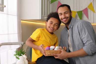 Photo of Happy African American father and his cute son with Easter eggs in kitchen