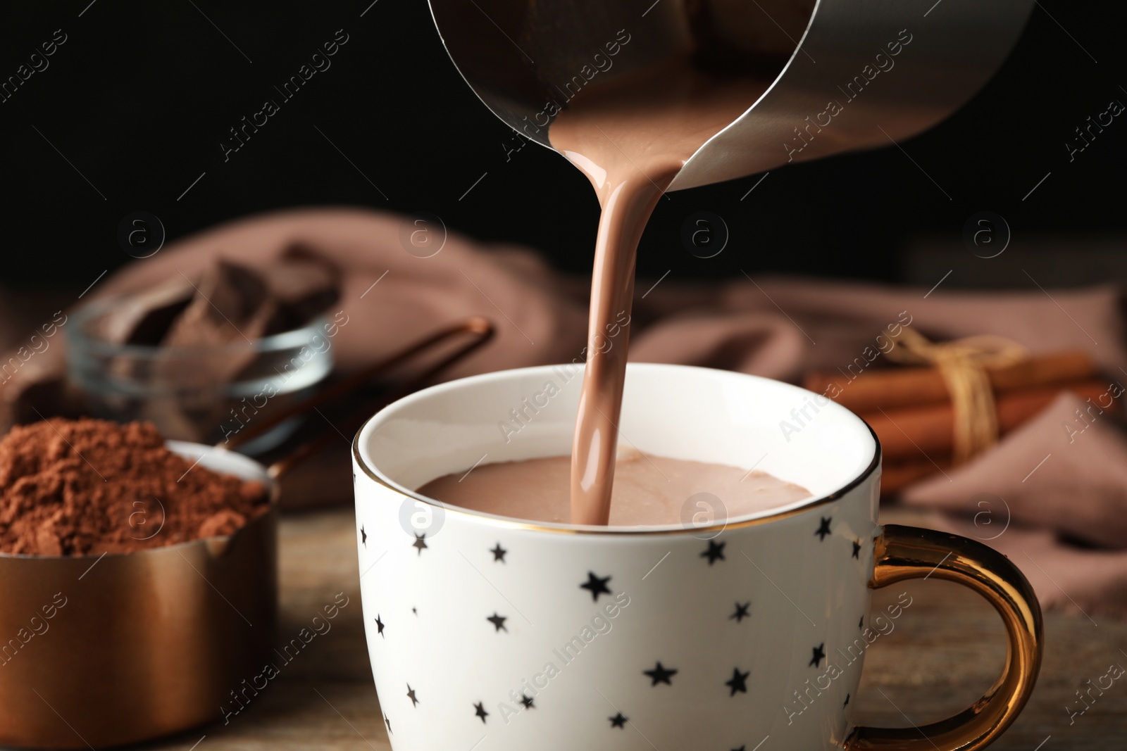 Photo of Pouring hot cocoa drink into cup on wooden table