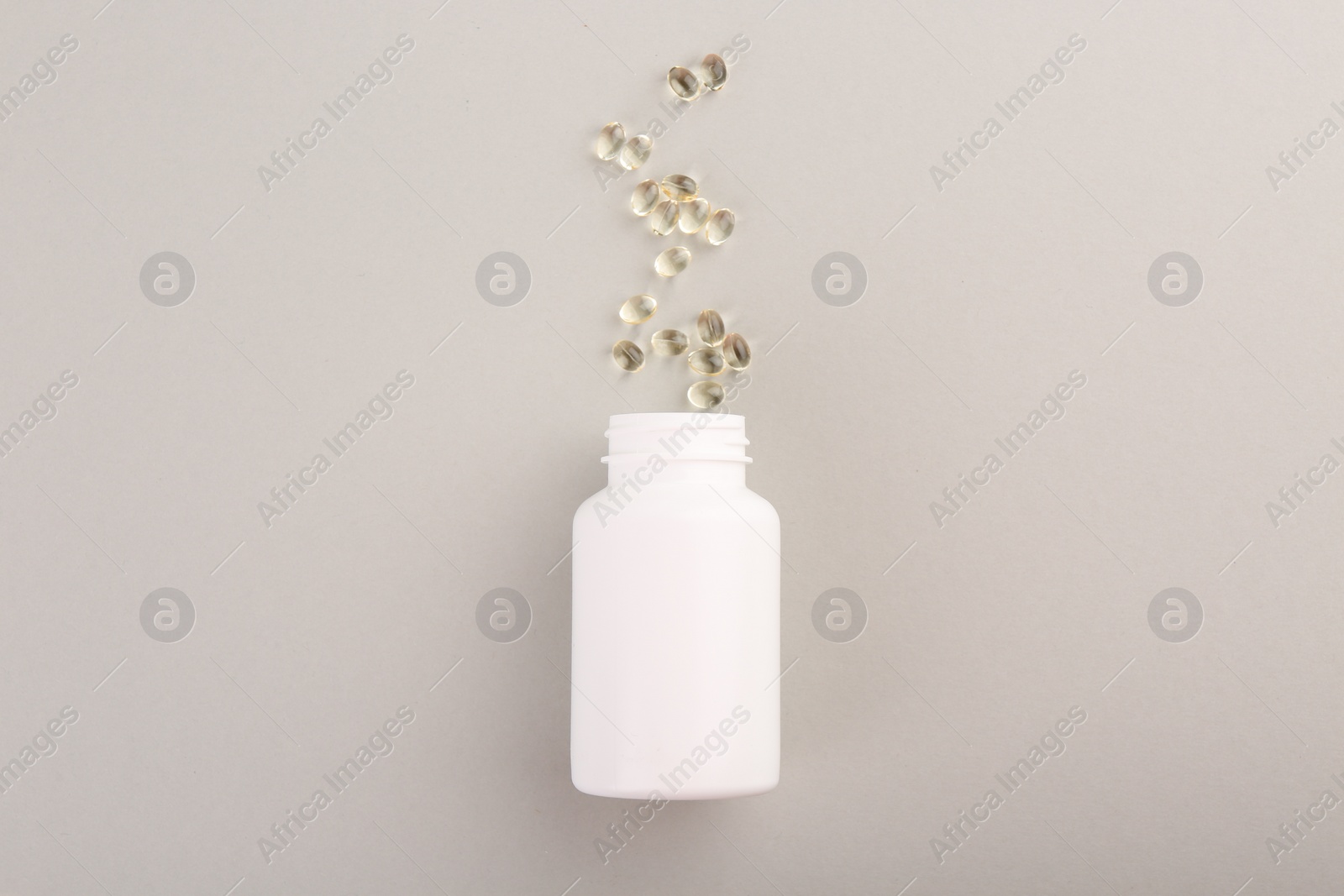 Photo of Bottle and vitamin capsules on light grey background, top view