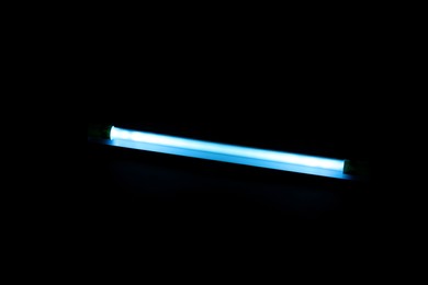 Photo of Modern ultraviolet lamp glowing on black background
