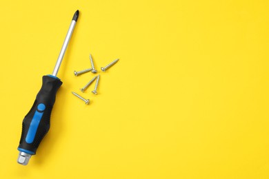 Photo of Screwdriver with black handle and screws on yellow background, flat lay. Space for text