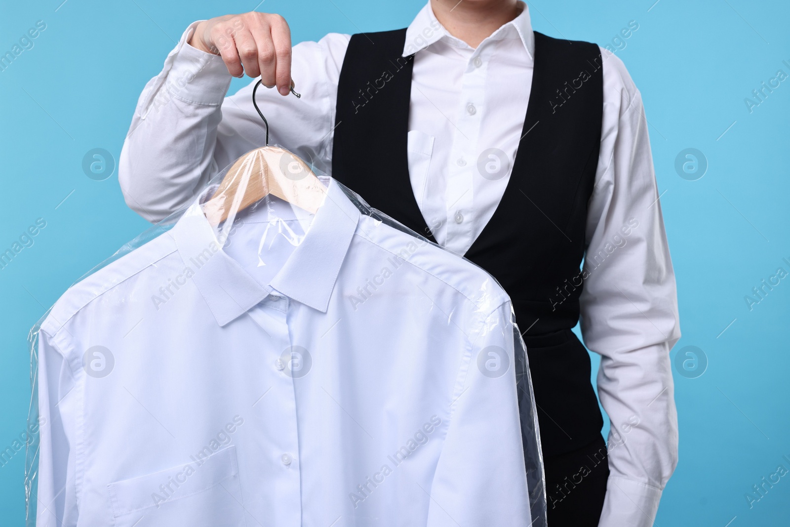 Photo of Dry-cleaning service. Woman holding shirt in plastic bag on light blue background, closeup