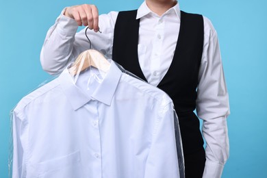 Photo of Dry-cleaning service. Woman holding shirt in plastic bag on light blue background, closeup