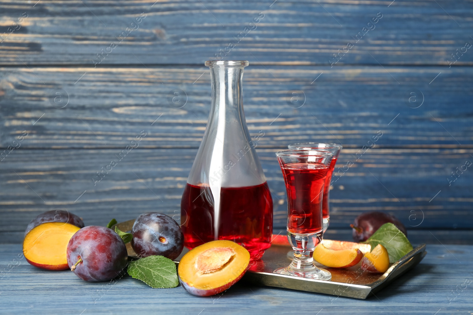 Photo of Delicious plum liquor and ripe fruits on blue wooden table. Homemade strong alcoholic beverage