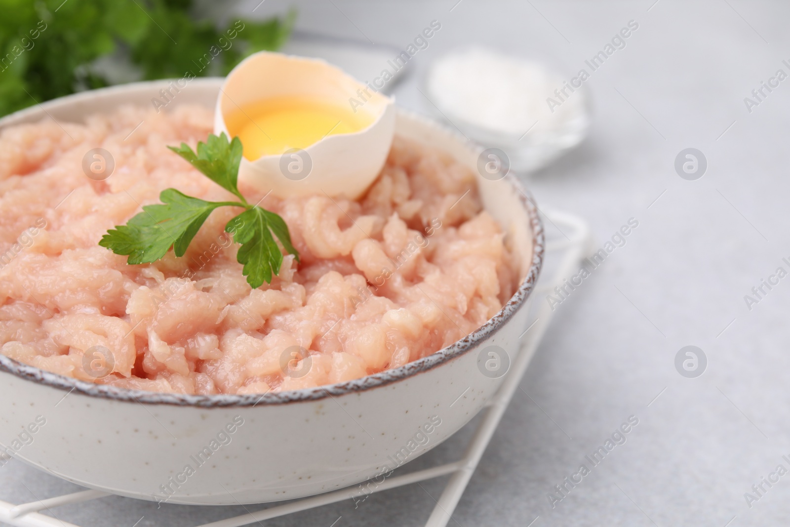 Photo of Fresh raw minced meat, parsley and egg in bowl on light grey table, closeup. Space for text