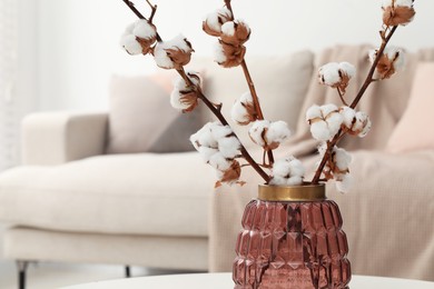 Photo of Cotton branches with fluffy flowers on white table in cozy room. Space for text