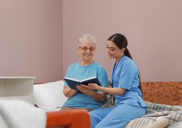 Photo of Nurse reading book with senior woman in hospital ward. Medical assisting