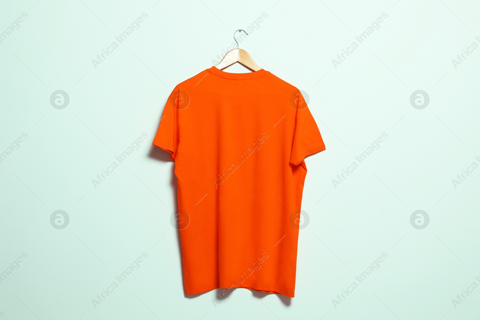 Photo of Hanger with orange t-shirt on light wall. Mockup for design