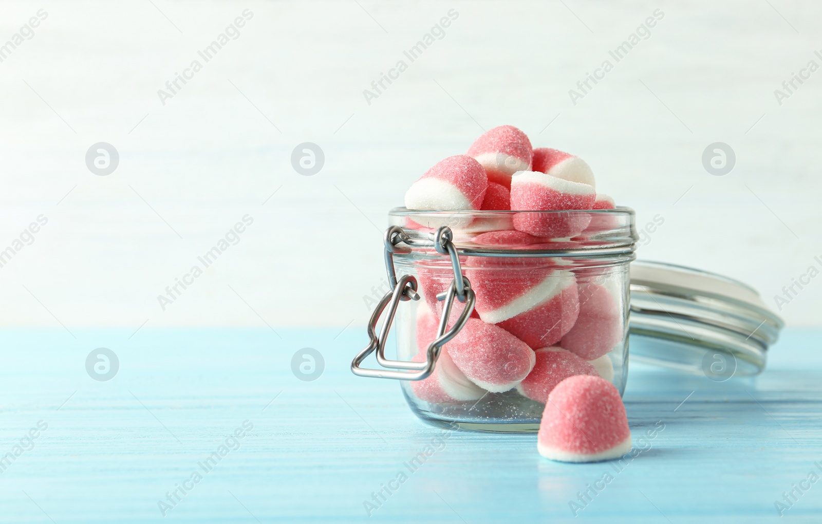 Photo of Glass jar with tasty jelly candies on blue wooden table against white background, space for text