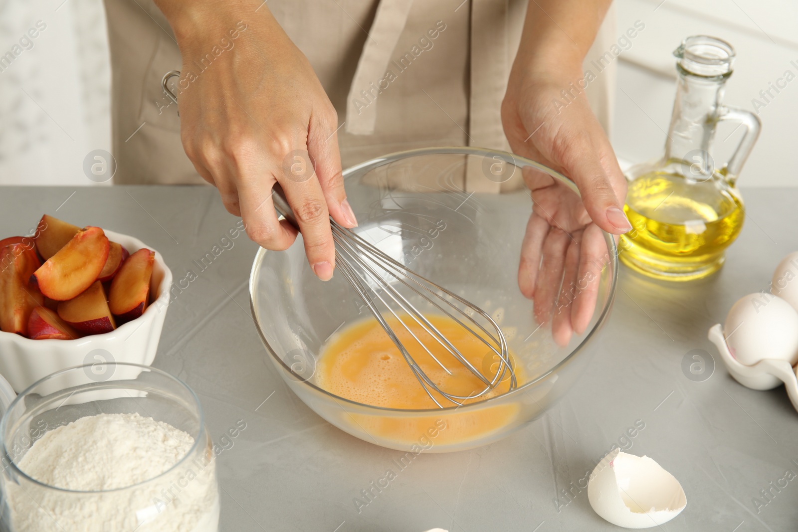 Photo of Woman whipping eggs at grey table, closeup. Cooking of delicious cake