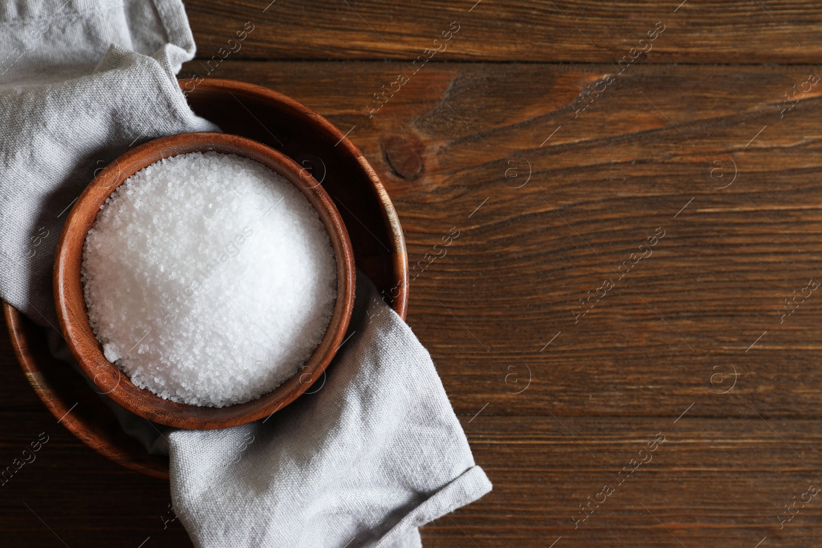 Photo of Organic salt in bowl on wooden table, top view. Space for text