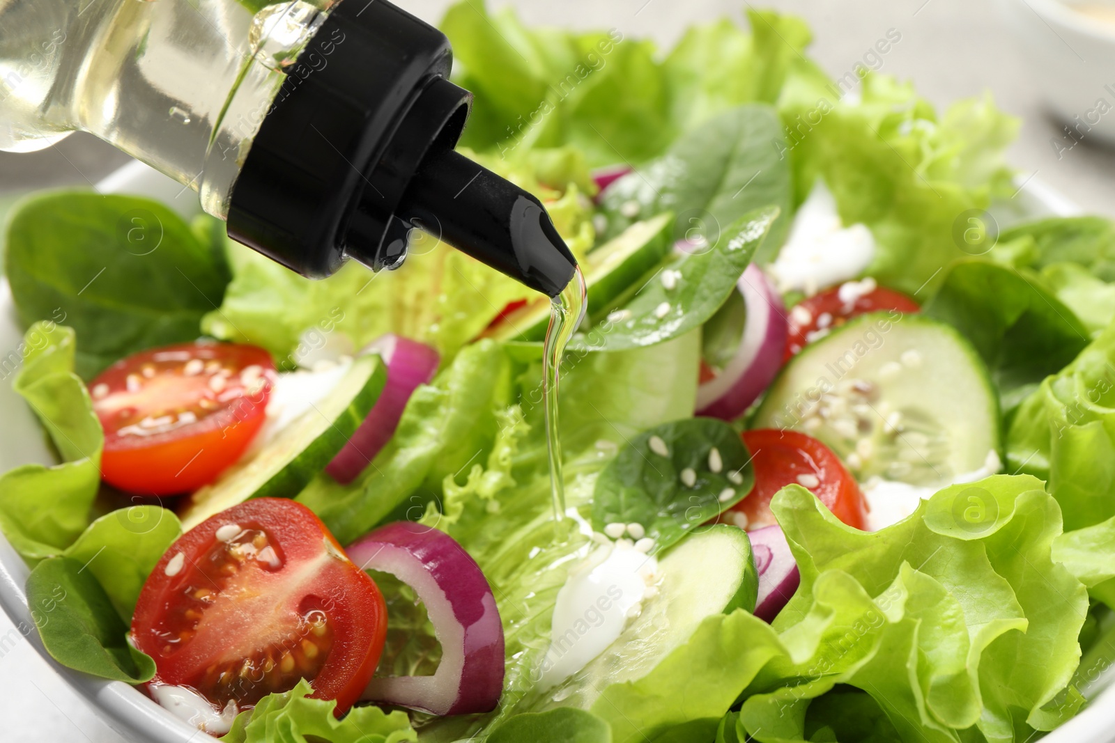 Photo of Pouring oil into delicious salad in bowl, closeup