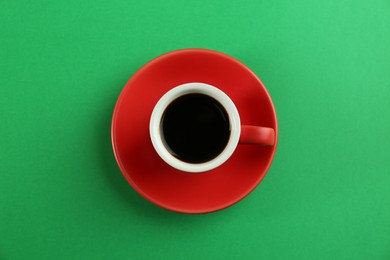 Cup of tasty coffee on green background, top view